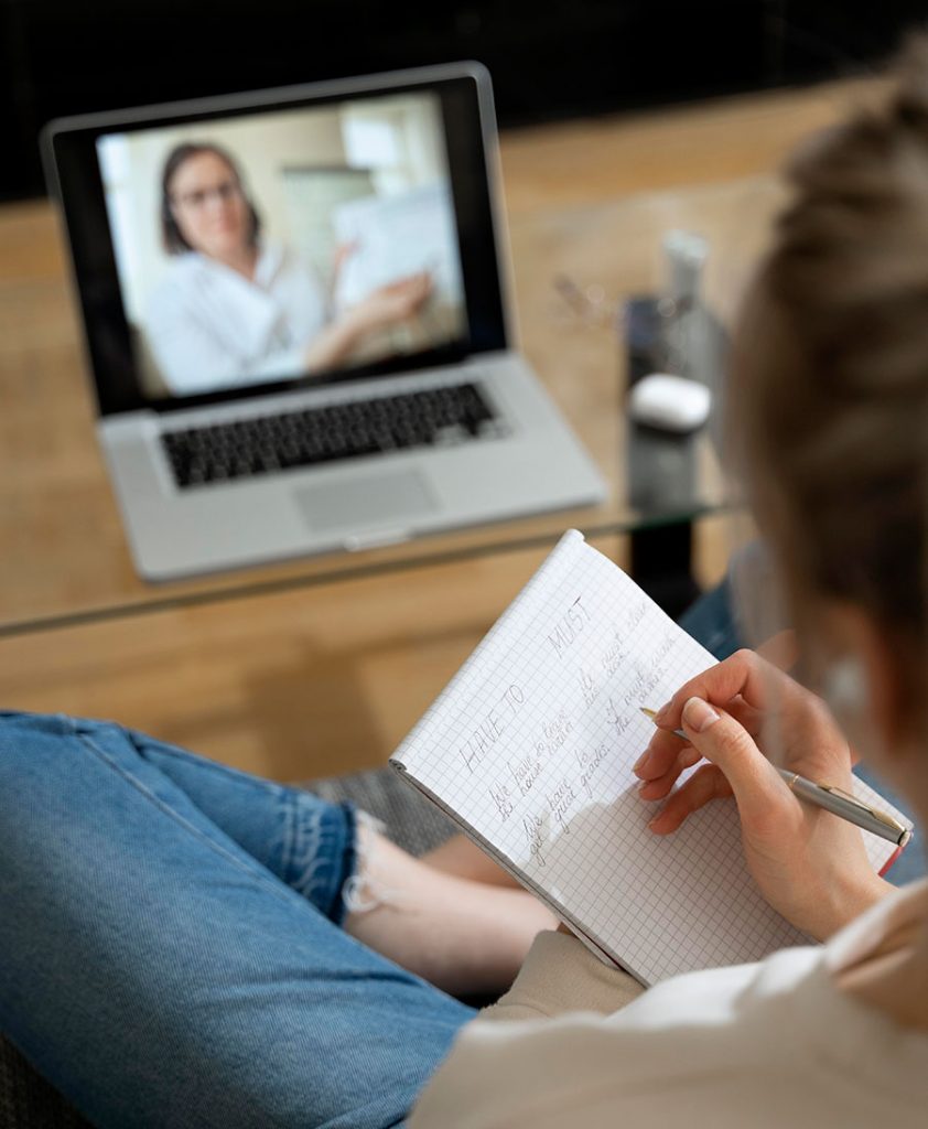 una chica toma apuntes de psicología en medio de una sesión de psicología online a través del portátil